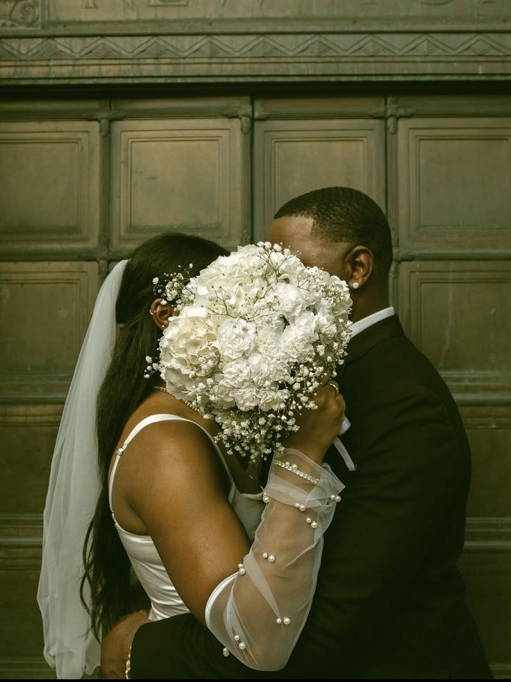 A bride and groom sharing a tender moment behind a white bridal bouquet