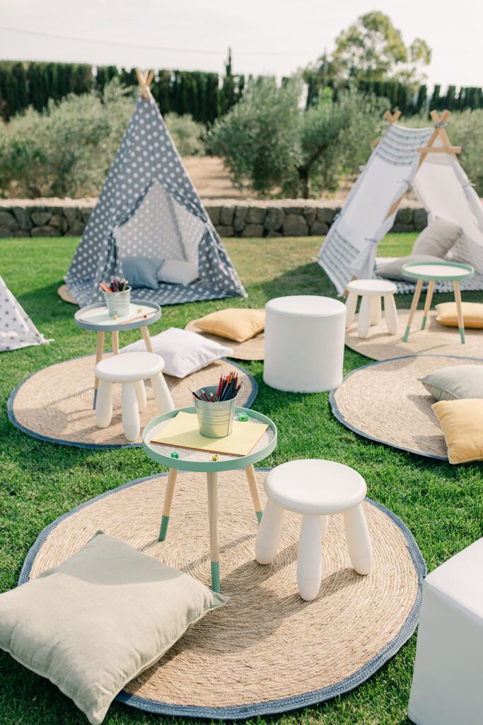 Children's teepees, round rugs and craft tables set up on a garden lawn.