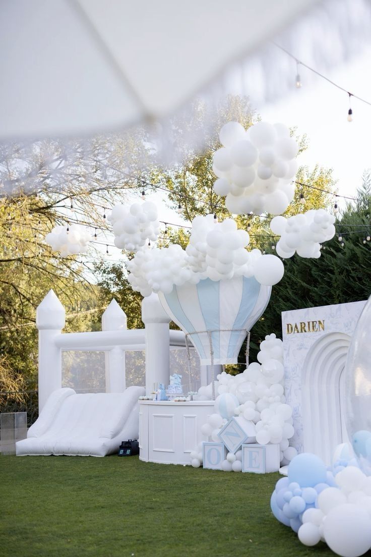 White bounce castle and pastel balloon installation styled for a celebration on a lawn.