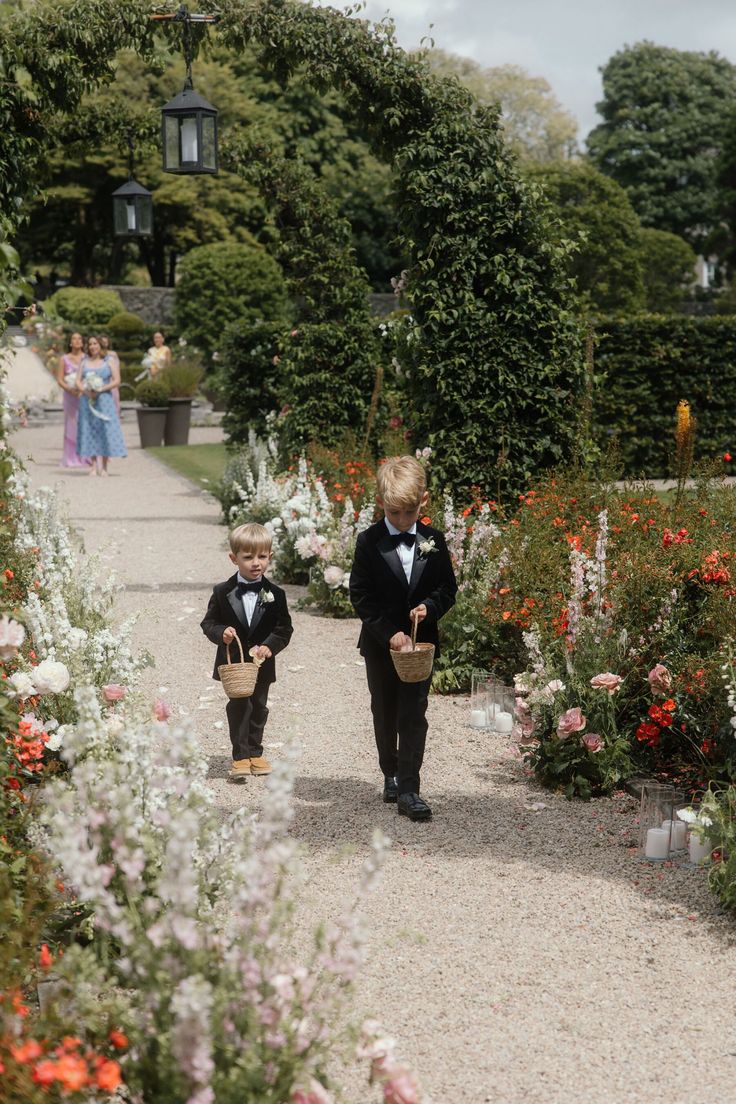 Two page boys in tuxedos carrying confetti baskets down a garden aisle