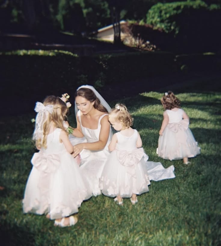 Bride kneeling on the lawn with flower girls in blush-sashed dresses