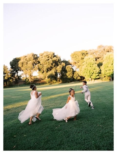 Children in wedding attire playing on the lawn at a farm wedding